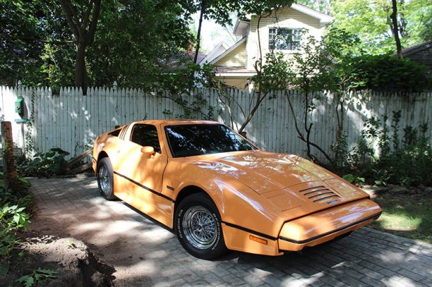 Bob’s vintage, orange Bricklin car is parked near the barn where a horse and carriage once resided.