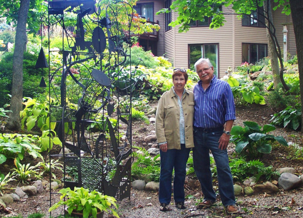 Kay and Michael Maitner stand in the woodland garden next to a metal sculpture titled “Kinetic Mandala" by Steven Spiegel.